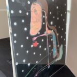 A whimsical, abstract painting on a black background with white polka dots, featuring a stylized figure holding a red bucket.