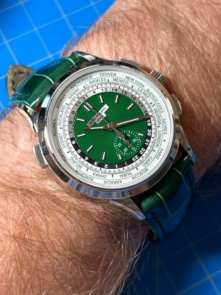 A close-up of a Patek Philippe World Time watch with a green dial and green alligator strap on a wrist.