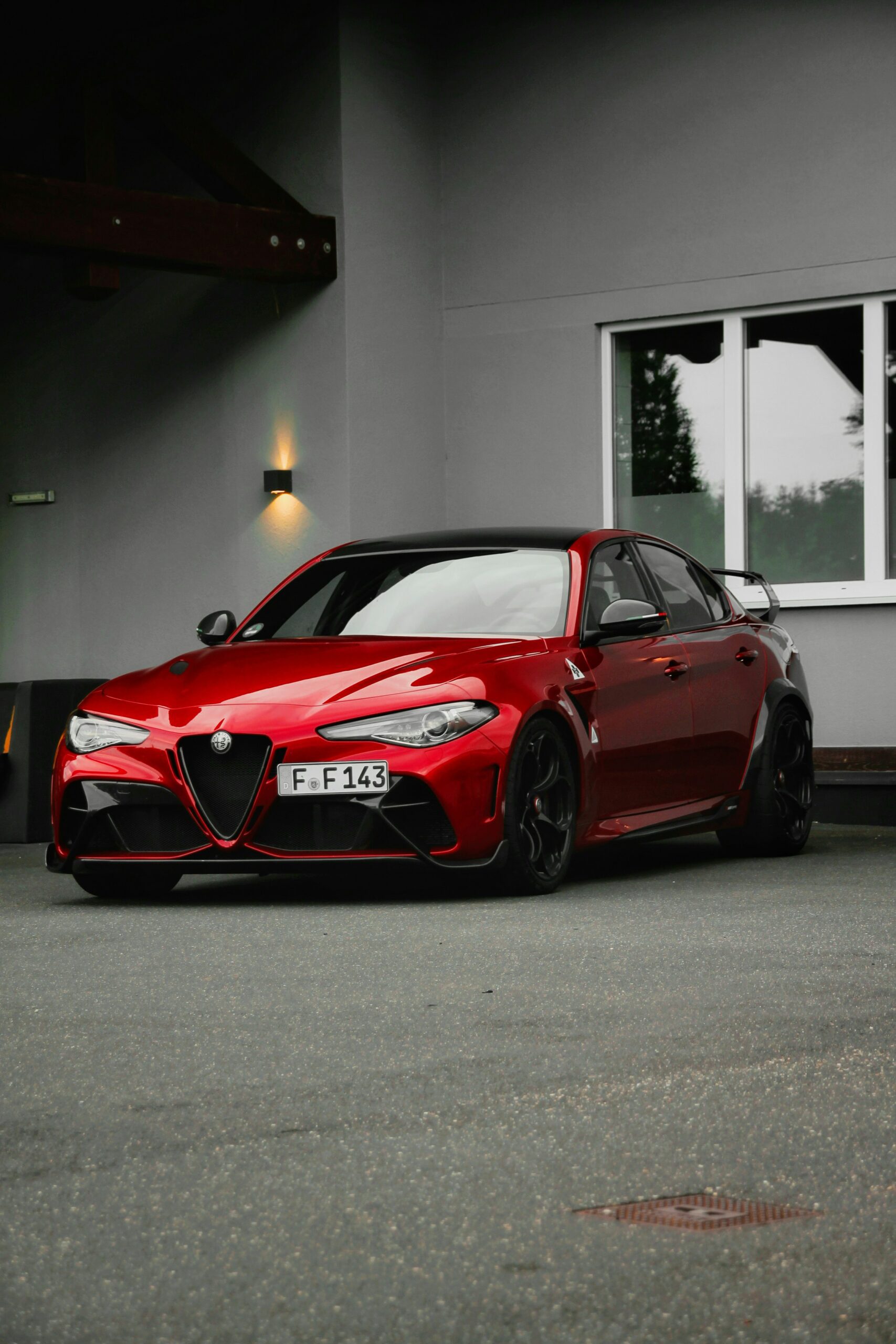 A sleek red Alfa Romeo Giulia parked outside a modern building with large windows.