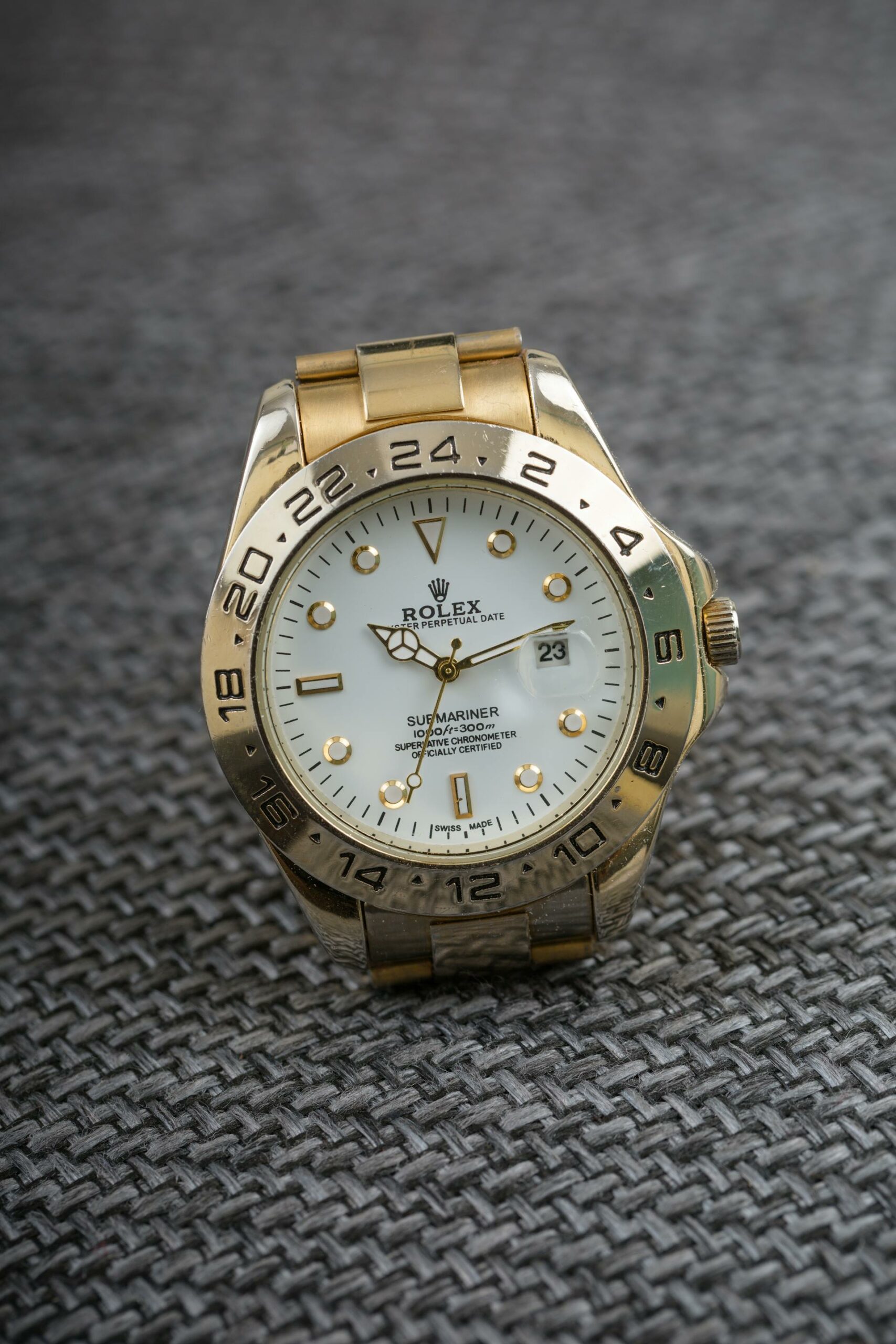 A close-up of a gold Rolex Submariner watch with a white dial and gold hour markers, resting on a gray textured surface.