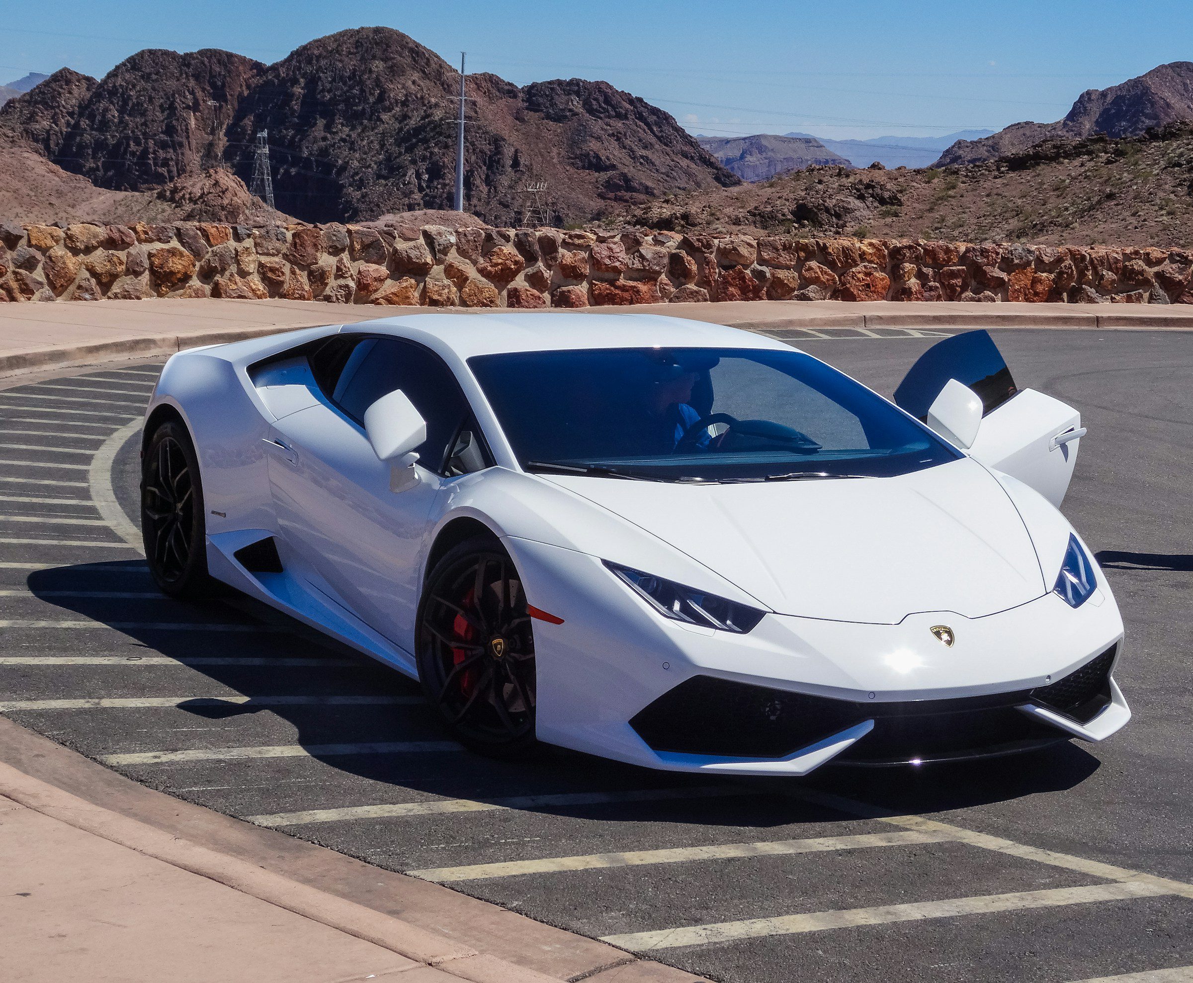 A white Lamborghini Huracan parked on an asphalt lot with mountains in the background.