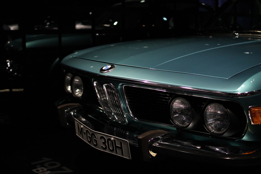 Front view of a teal vintage bmw with dual round headlights and chrome grille at night, license plate m-gg 30h visible; car on display in a dark setting.