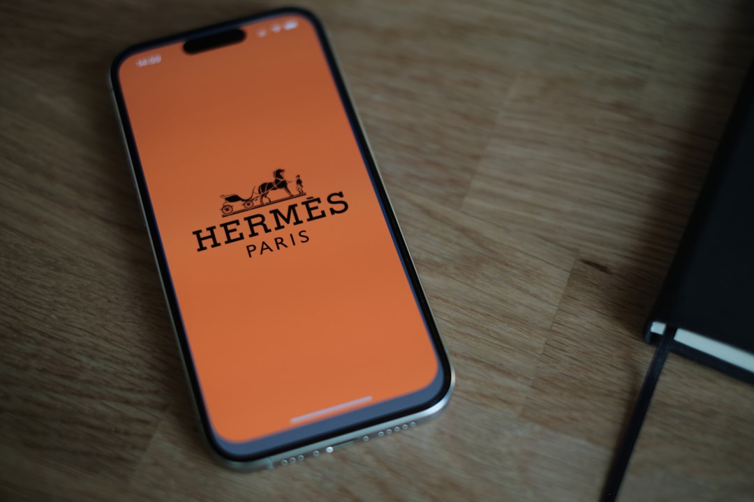 Iphone lying on a wooden desk with an orange screen displaying the hermès paris logo