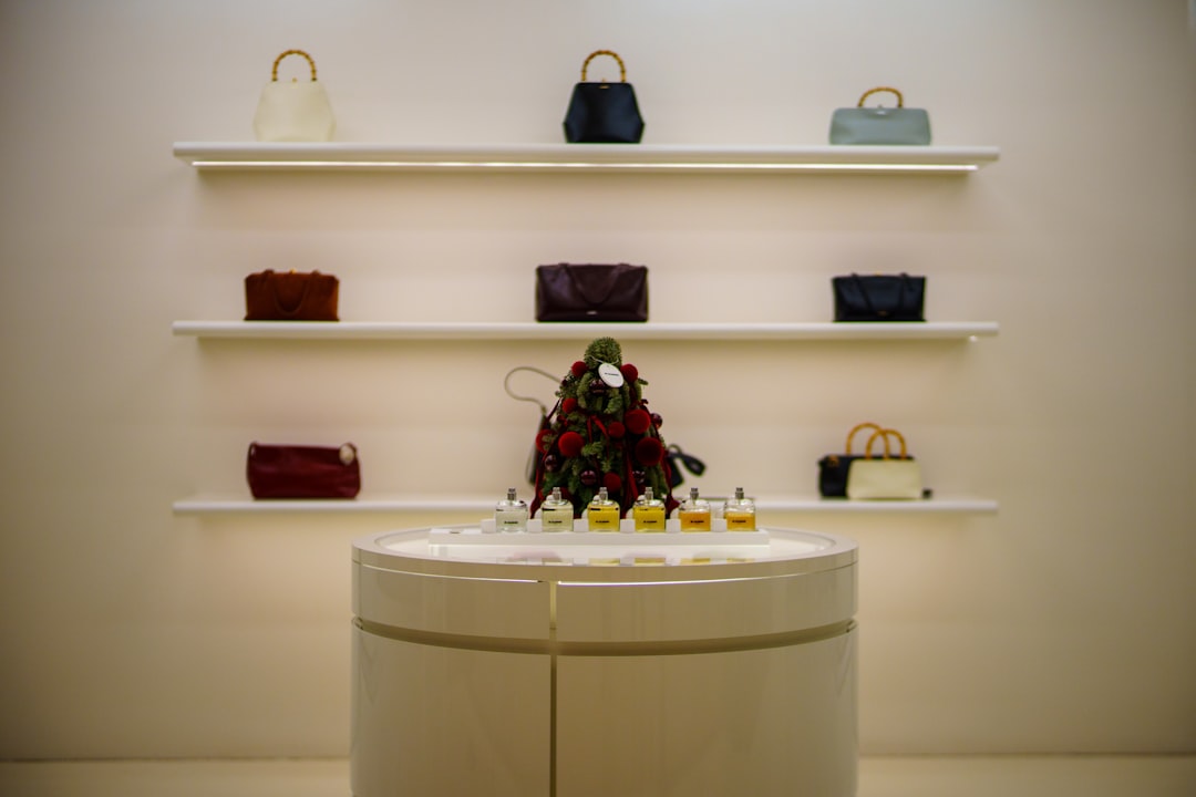 Hermes-handbag-history-birkin-kelly-value - borro - borro Boutique display: white shelves hold assorted handbags; a round white pedestal showcases small perfume bottles with a festive centerpiece in the middle.