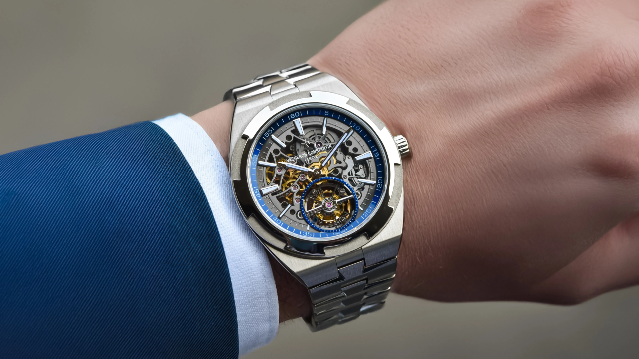 Loan-against-vacheron-constantin - borro Skeleton wristwatch with visible gears and a blue-accented bezel on a stainless steel bracelet, worn on a blue suit sleeve.
