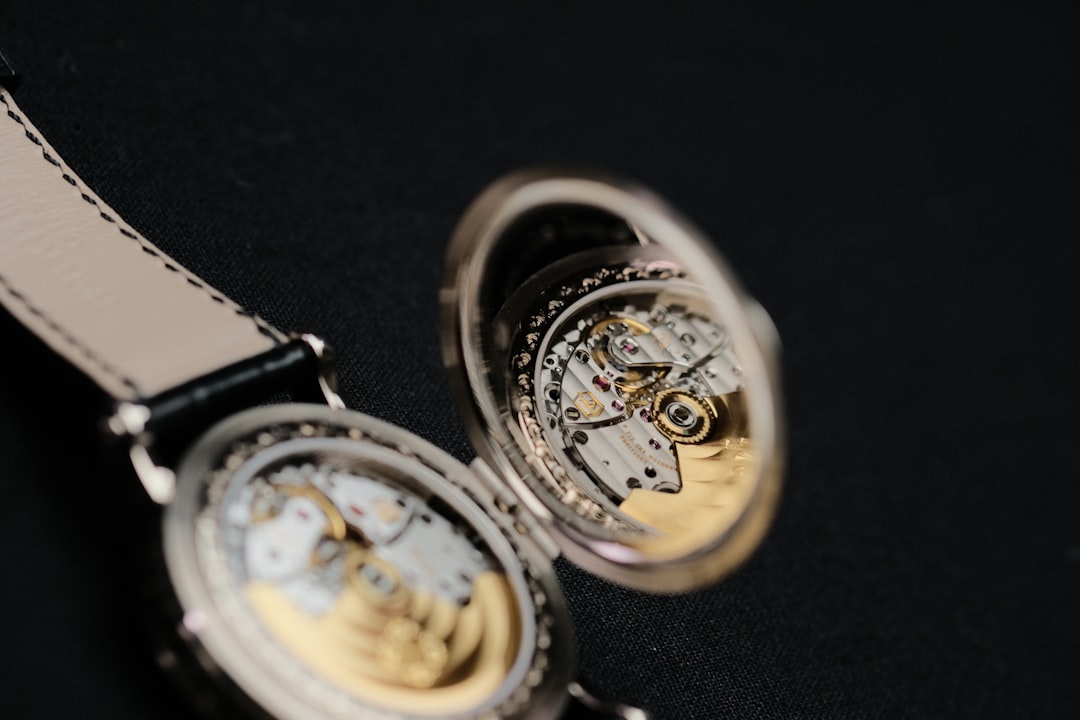 Close-up of two open-pocket watches showing intricate gears and gold rotor against a dark fabric background.