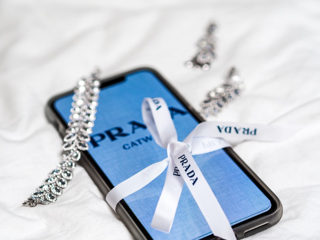 Blue Prada phone case wrapped with a white ribbon, surrounded by silver jewelry on a white surface