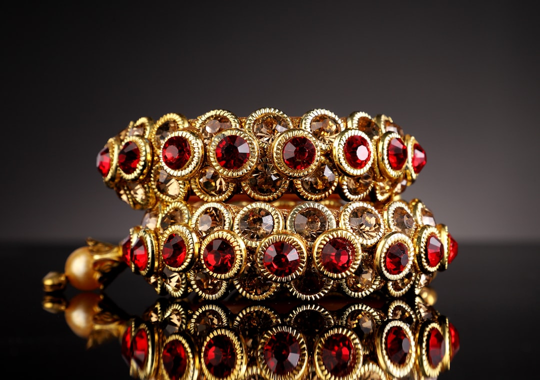 Gold-tone bracelet with repeating circular settings each containing a red gem, on a reflective surface.