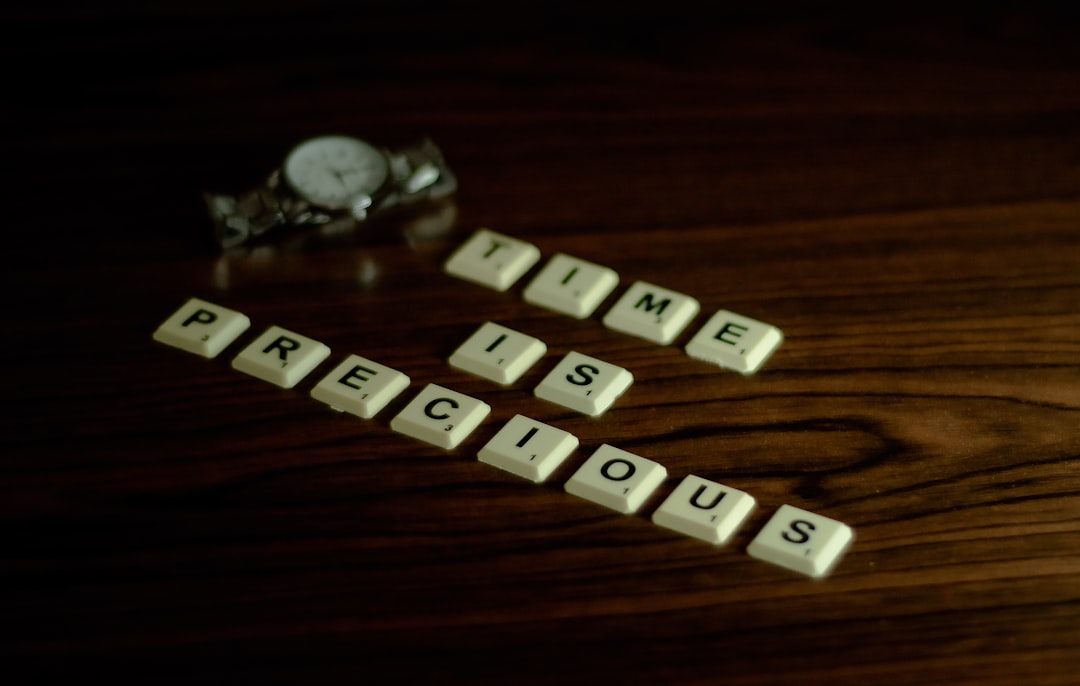 Scrabble tiles spell 'precious time' on a dark wooden table with a small pile of coins blurred in the background.