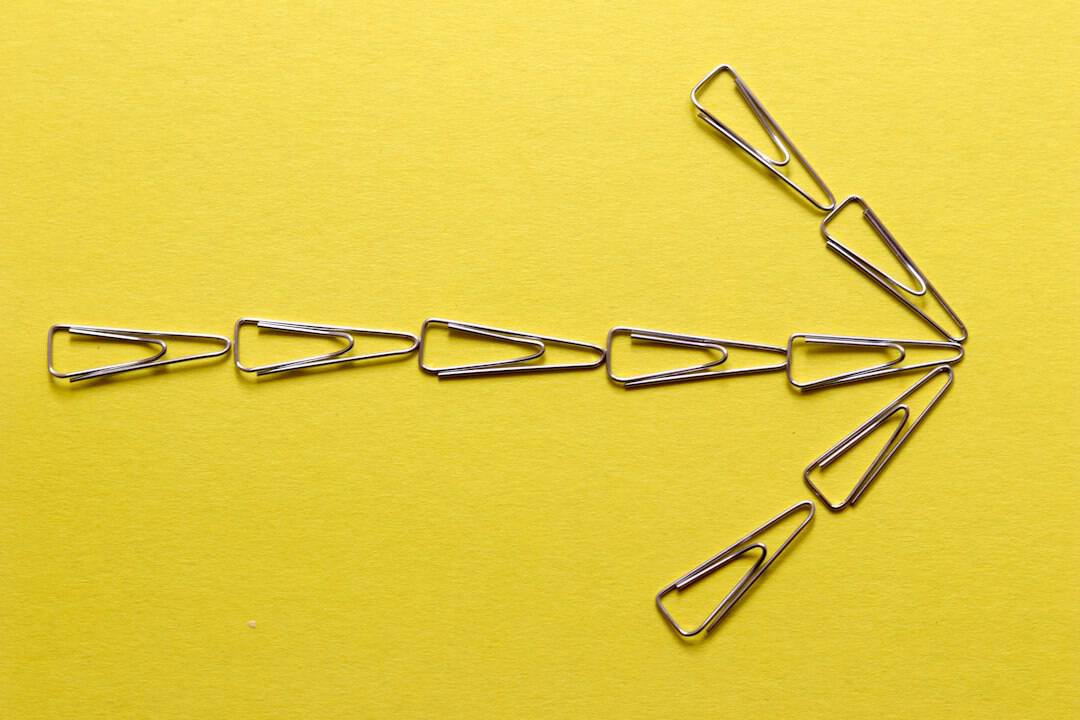 Paperclip arrow pointing right on bright yellow surface for creative design.