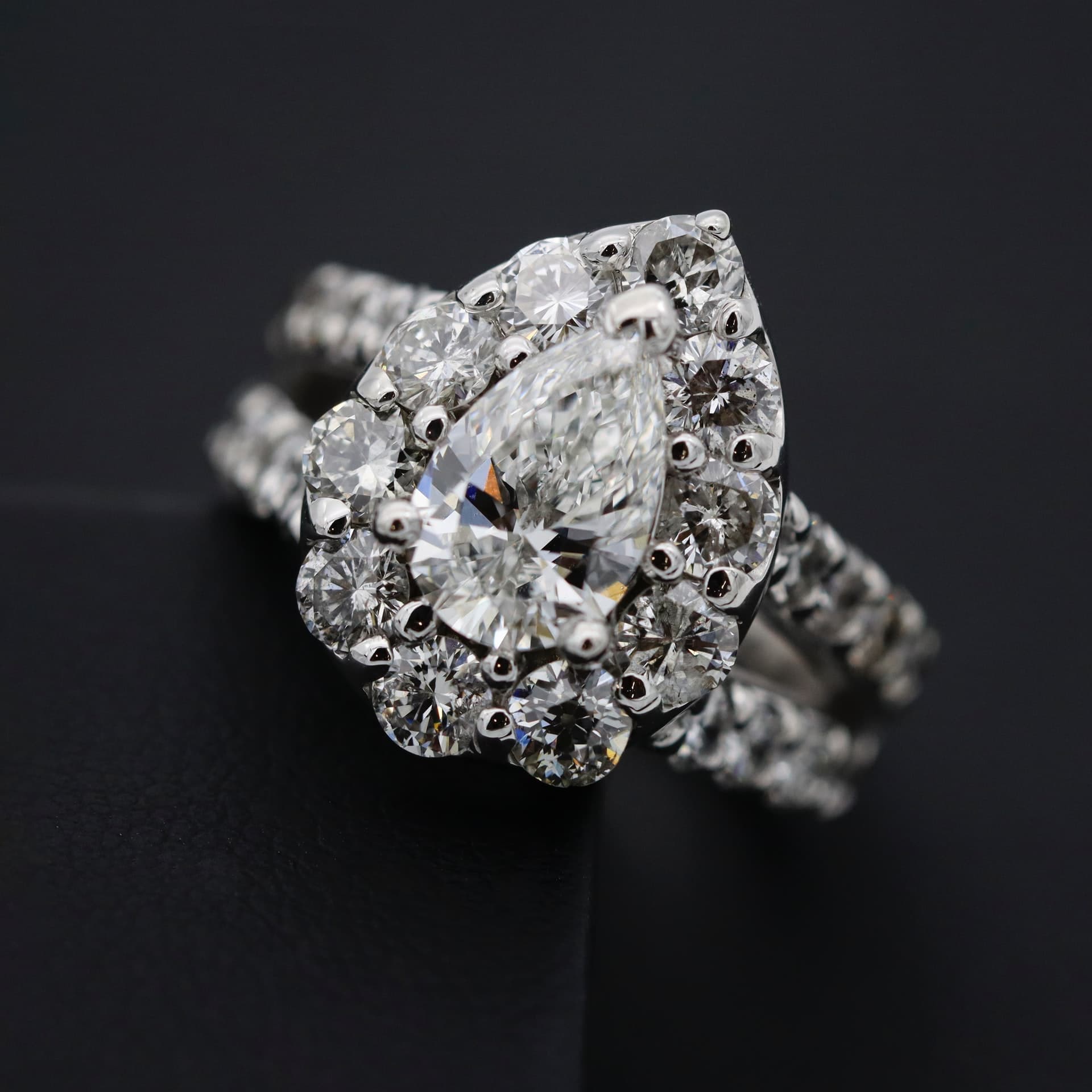 Luxury diamond ring with pear-shaped center stone and surrounding smaller diamonds.