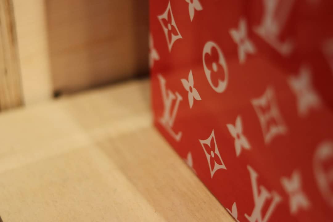 Red luxury storage box with Louis Vuitton pattern on a wooden surface.