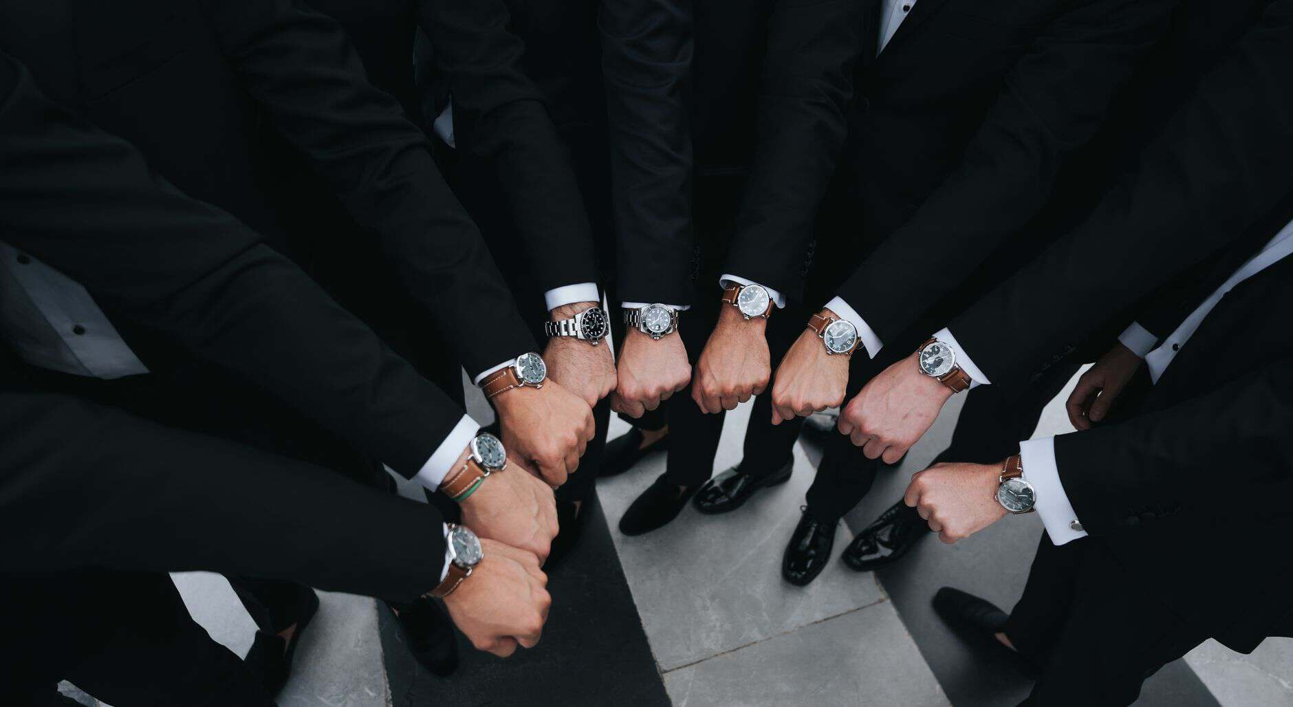 Group of men in suits showing off luxury watches on their wrists.