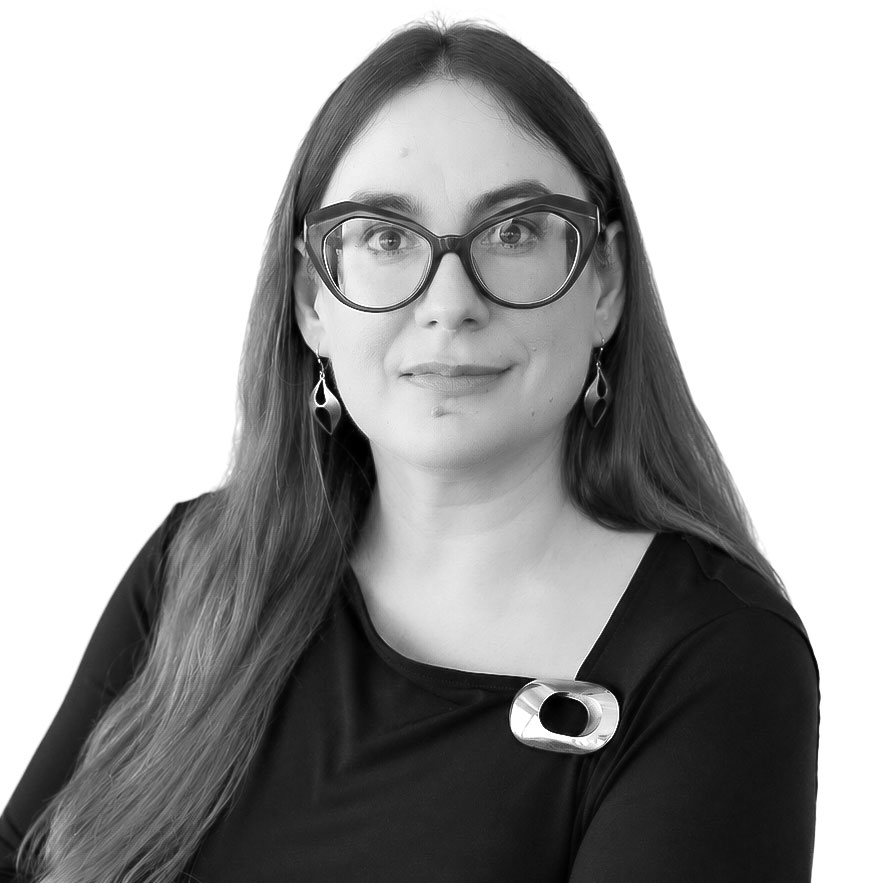 Professional portrait of a woman wearing glasses, black top, and a decorative pin.